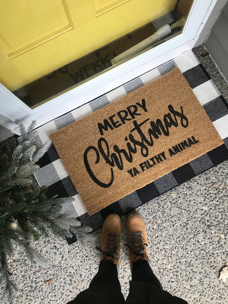 a person standing in front of a door with a merry christmas ya filthy animal mat