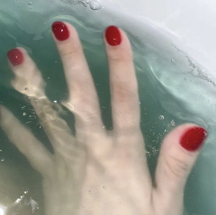 a woman's hand with red nail polish in water