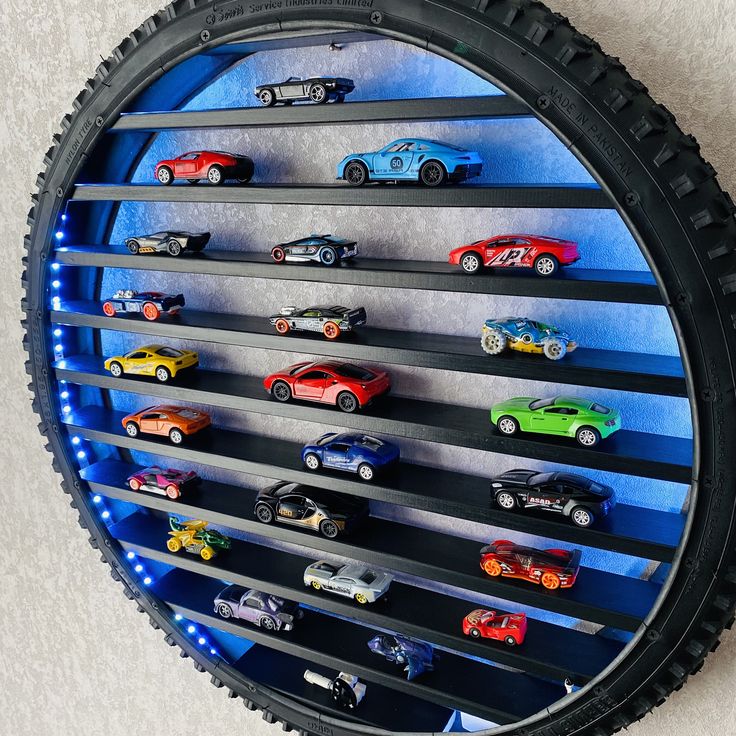 there are many toy cars on display in the tire rim wall shelf that is lit up with blue lights