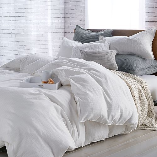 an unmade bed with white sheets and pillows on top of it in front of a brick wall