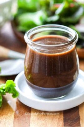 a small glass jar filled with sauce on top of a white plate next to a salad