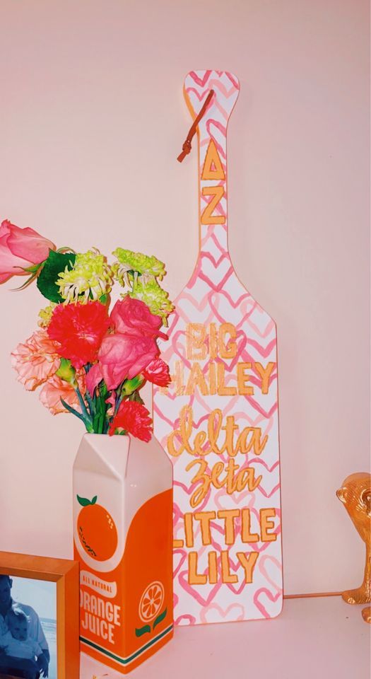 flowers in a vase next to an orange juice carton and a pink bottle shaped like a giraffe