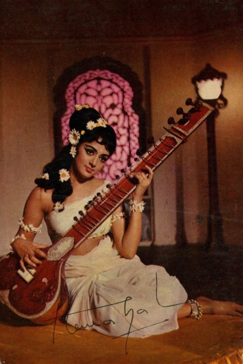 a woman sitting on the ground holding a guitar in her hand and wearing a flowered headdress