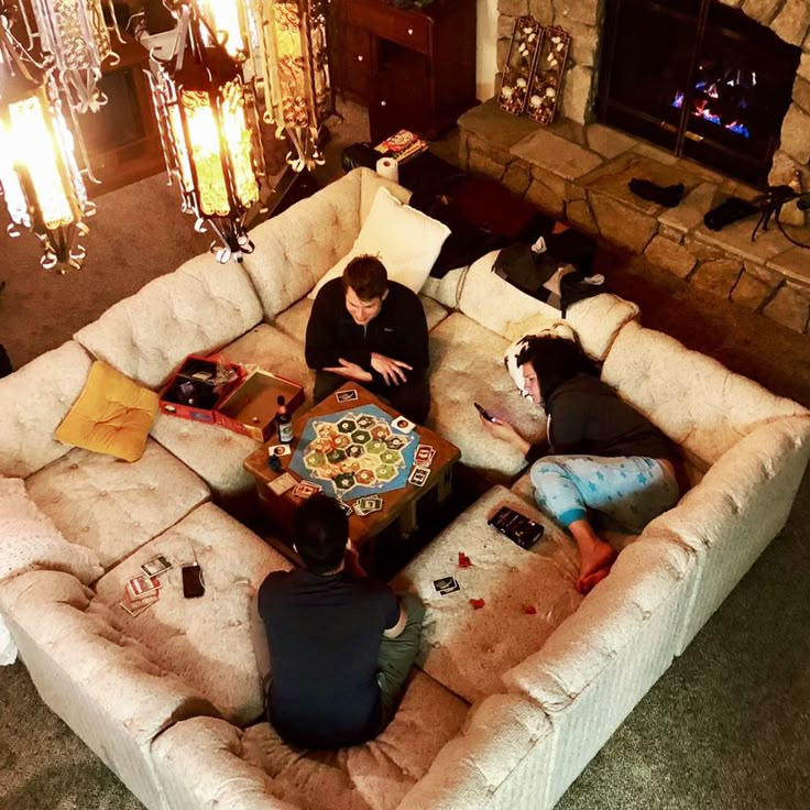 three people sitting on a couch in front of a fire place with a game table