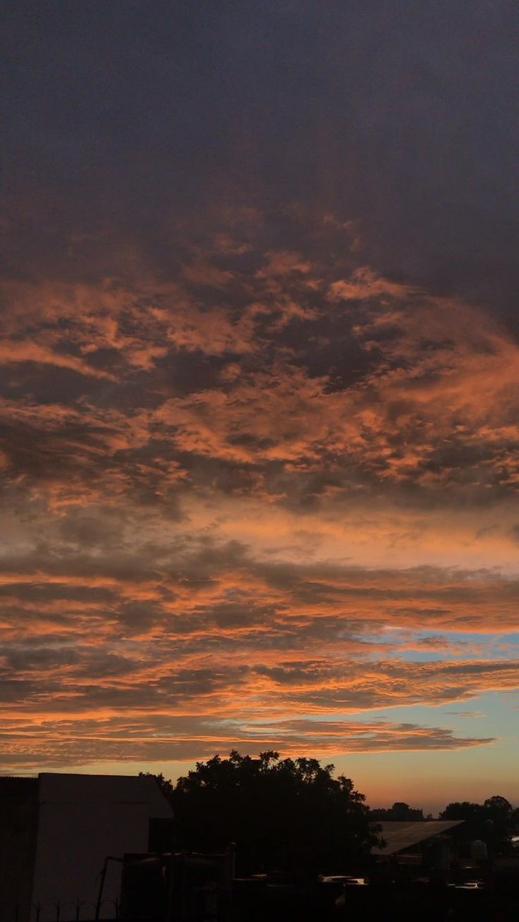 the sky is filled with colorful clouds as the sun sets in the distance behind some buildings