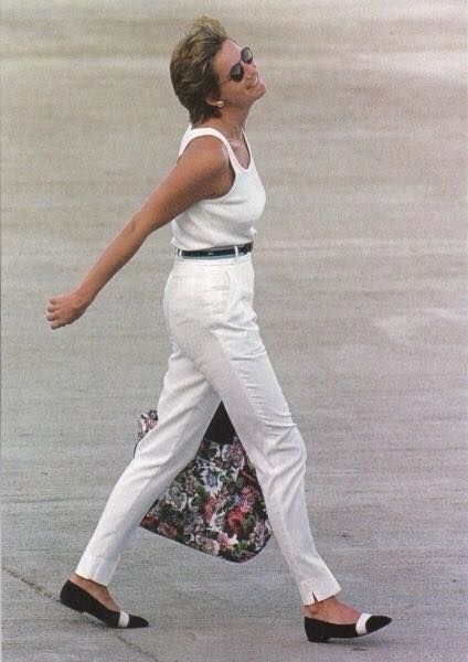 a woman walking down the street with her handbag in her mouth and wearing white pants