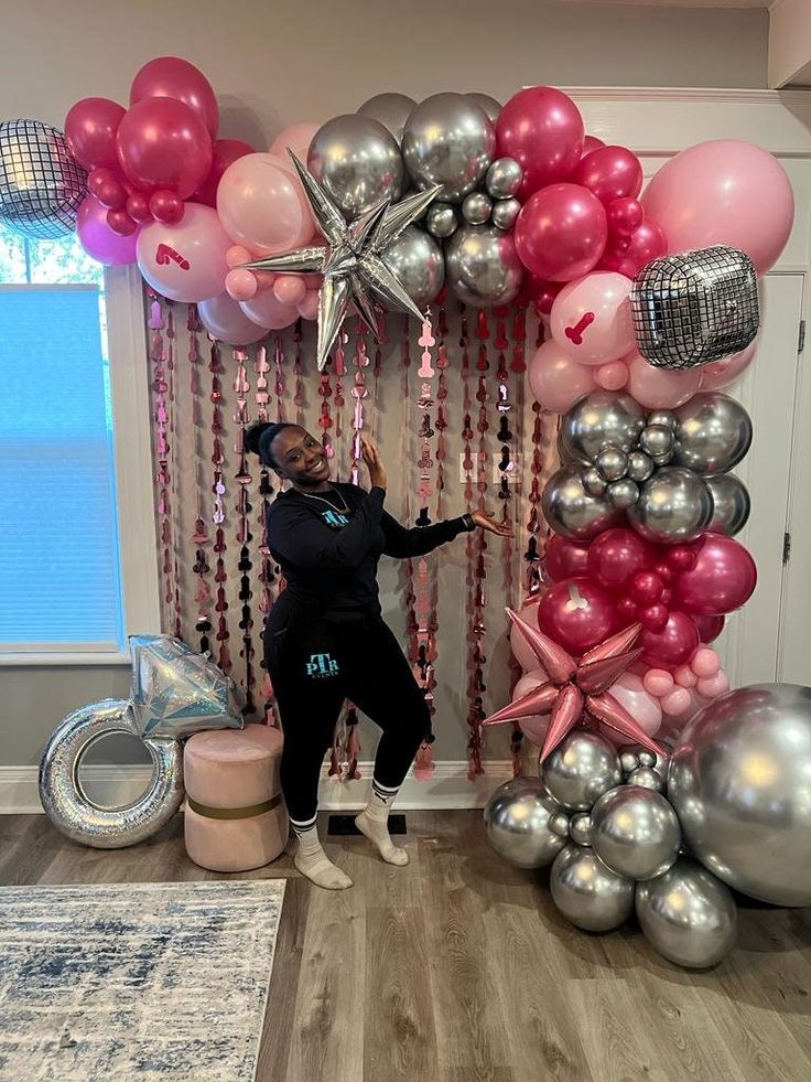 a woman standing in front of a balloon arch with pink and silver balloons on it