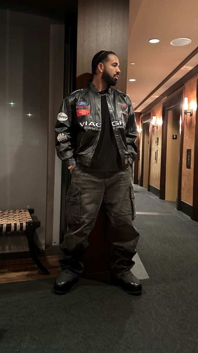 a man standing next to a wall in a hallway wearing a leather jacket and jeans