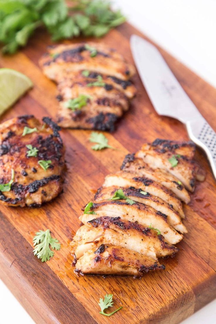 grilled chicken patties on a cutting board with cilantro and lime wedges