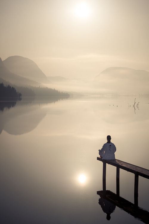 a person sitting on a dock looking out at the water with mountains in the background