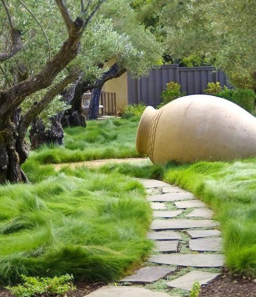 a stone path leading to a large rock in the middle of a garden with green grass