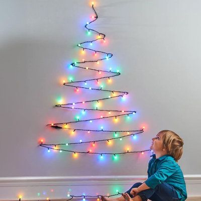 a young boy sitting on the floor in front of a christmas tree decorated with multicolored lights