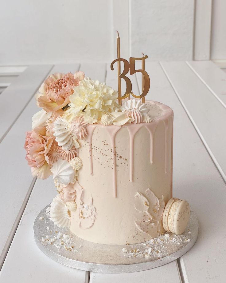 a white cake with flowers and a number on top is sitting on a wooden table