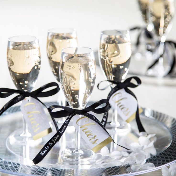 four champagne glasses are sitting on a silver tray with black ribbon around the wine glasses