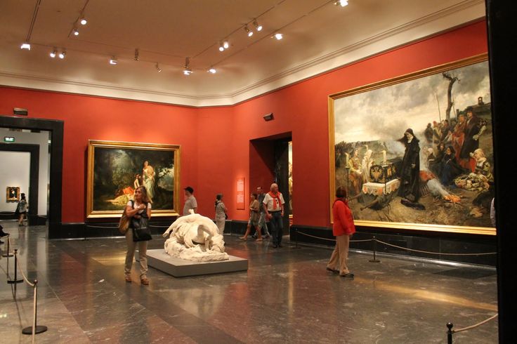 people are looking at paintings in an art museum with red walls and marble flooring