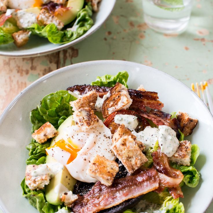 two white plates filled with bacon, eggs and lettuce on top of a table