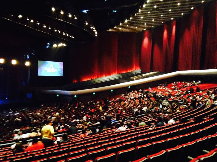 an auditorium filled with people sitting in red seats and watching a movie on the screen