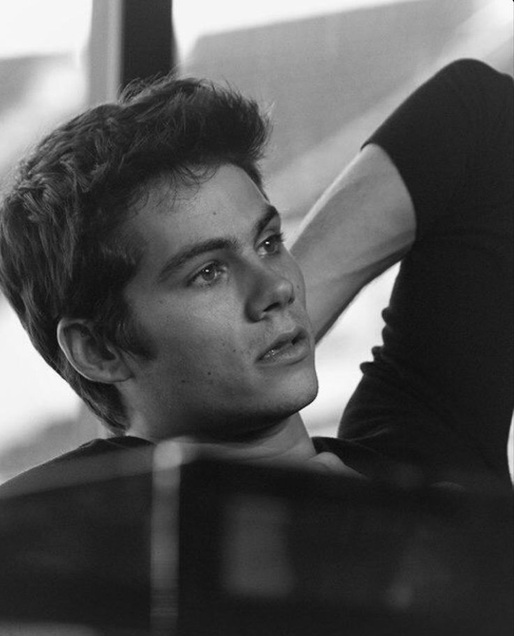 black and white photograph of a young man leaning against a wall with his hand on his head