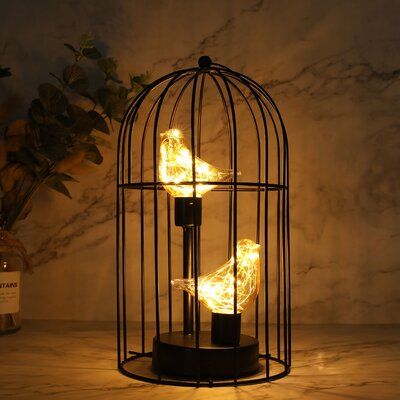 a bird in a cage that is lit up with some lights on top of it