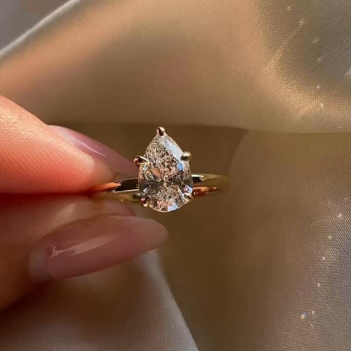 a woman's hand holding an engagement ring with a pear shaped diamond on it