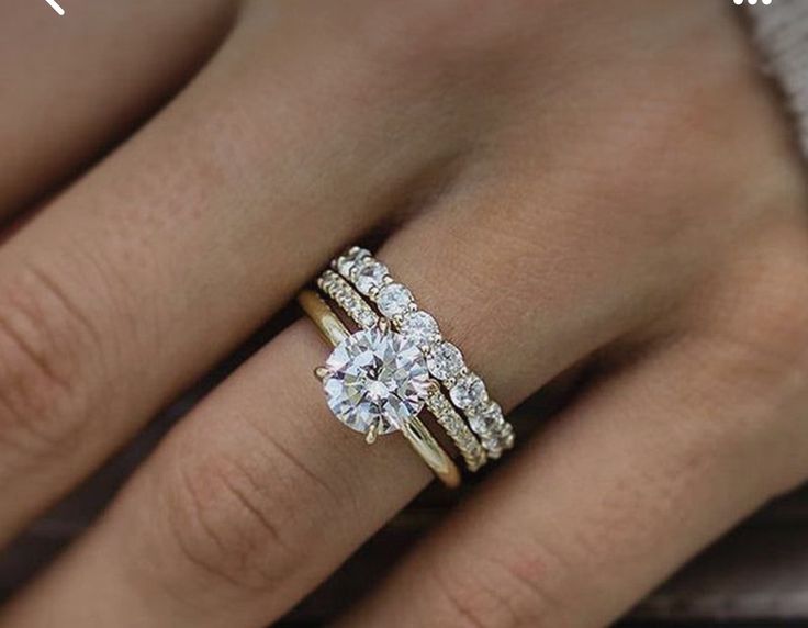 a woman's hand with two wedding rings on her left and the other hand holding an engagement ring