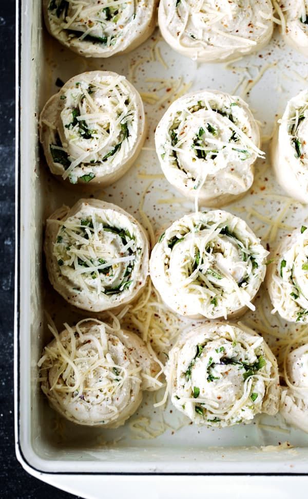 several rolls covered in cheese and spinach sprinkled with parmesan