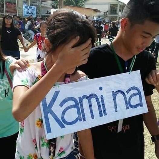 two people holding up a sign that says karmina in front of other people