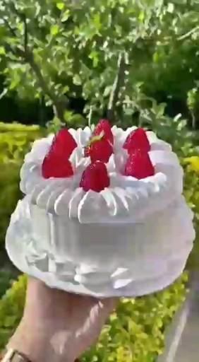 a hand holding a cake with strawberries on top