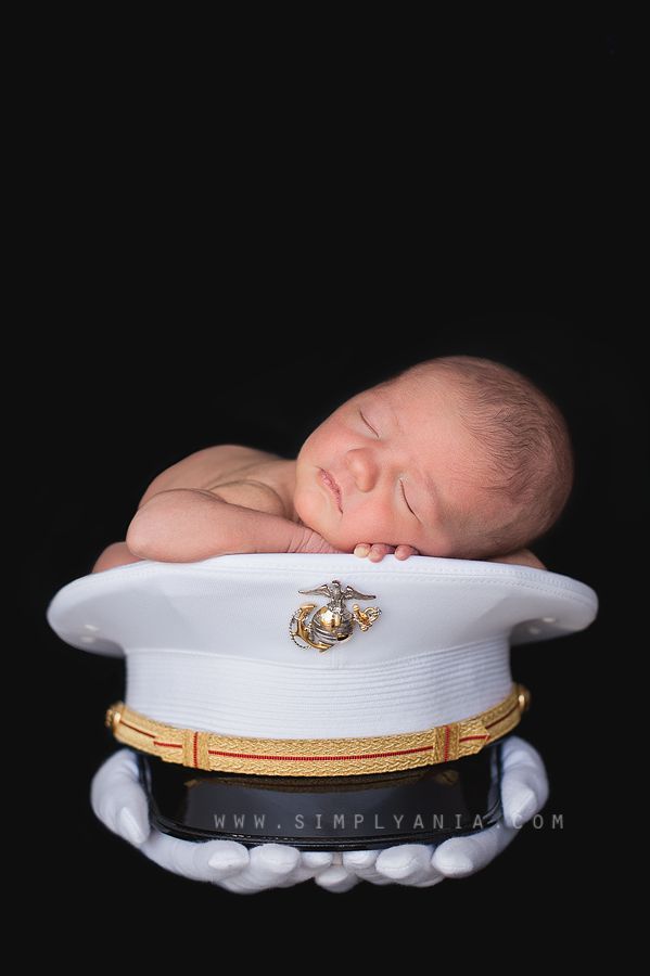 a newborn baby is sleeping on top of a navy officer's hat with his eyes closed