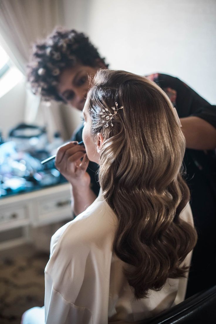 a woman is getting her hair done by another person in the mirror and she is wearing a tiara