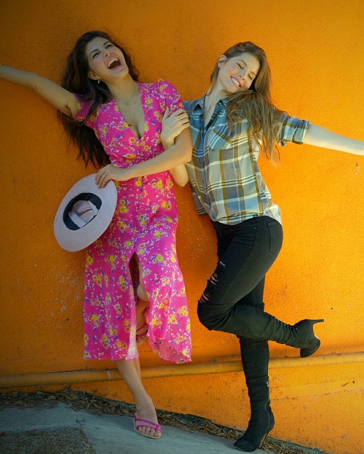 two young women standing next to each other in front of a yellow wall with their arms outstretched