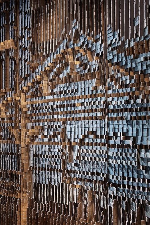 an abstract wood sculpture with blue and brown squares on it's sides, in front of a wooden wall