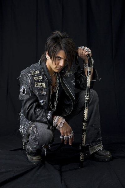 a man in black leather jacket and chain around his ankles posing for a photo on a black background