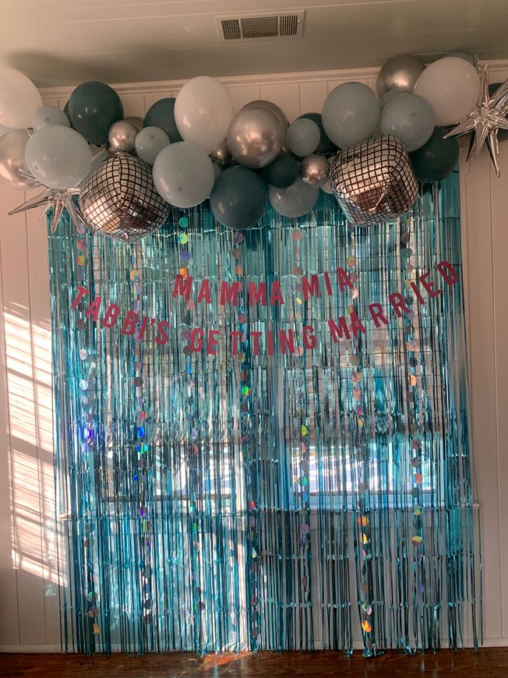 balloons and streamers are hanging from the ceiling in front of a curtain that says happy new year