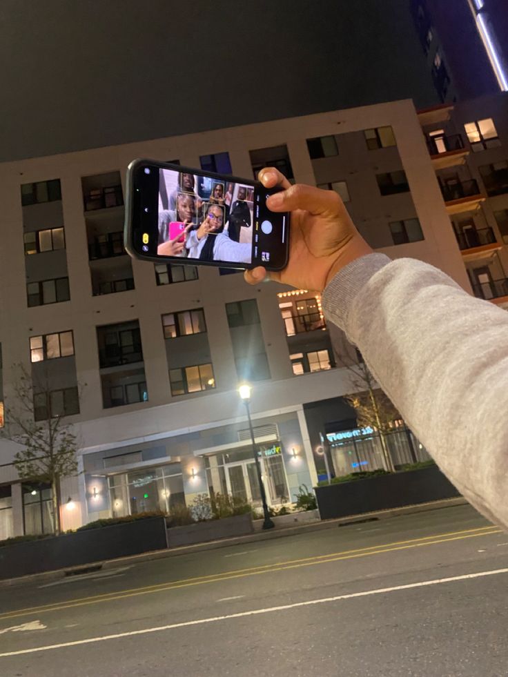 a person holding up a cell phone in front of a building at night with lights on