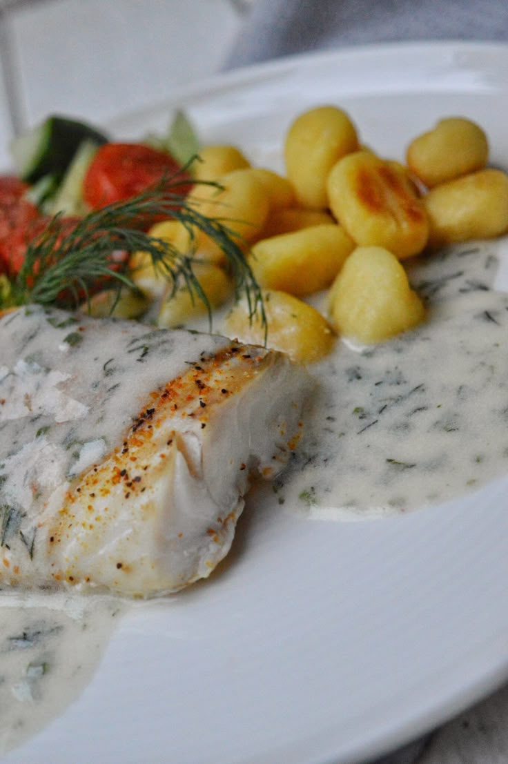 a white plate topped with fish covered in gravy next to potatoes and veggies