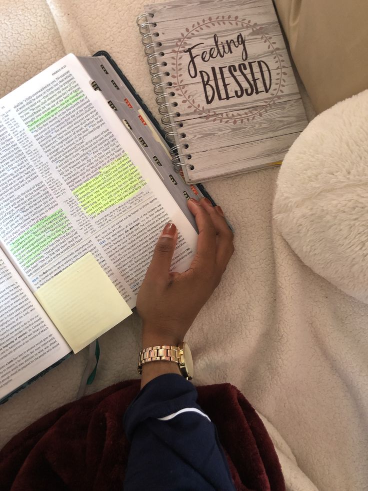 a person is reading a book while laying on the couch with their hand resting on an open bible