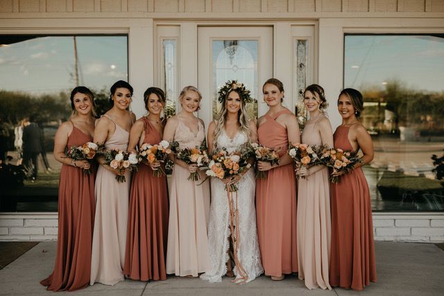 a group of women standing next to each other in front of a building holding bouquets