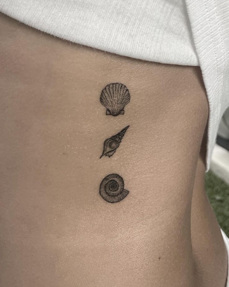 a woman's stomach with three seashells and a shell tattoo on it