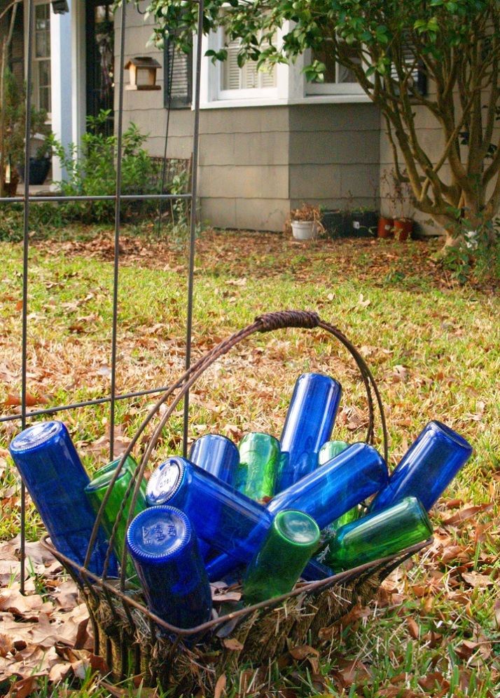 a basket filled with blue and green bottles sitting on top of leaves in front of a house