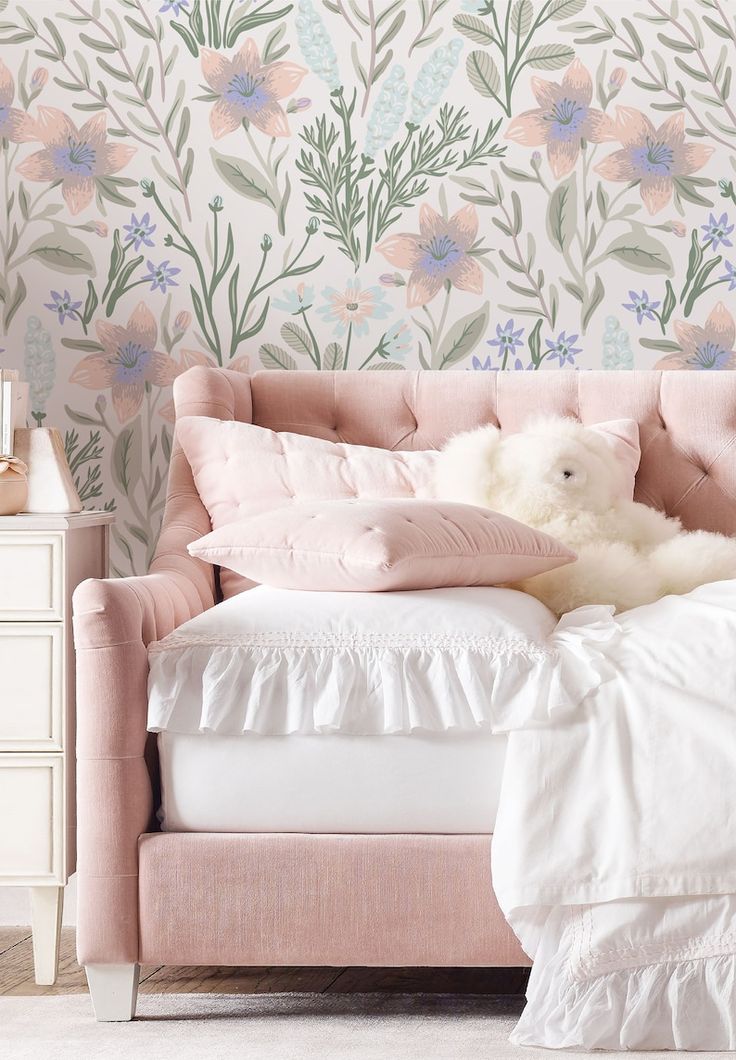 a white teddy bear sitting on top of a bed next to a floral wallpaper