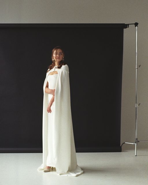 a woman in a white dress standing next to a black backdrop with a light on it