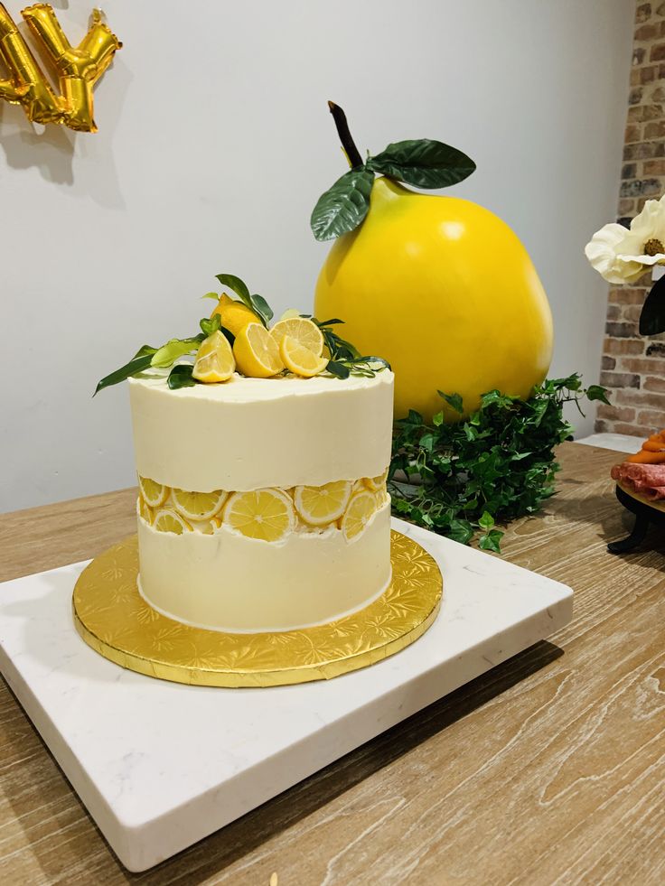 a white and yellow cake sitting on top of a table next to a giant lemon