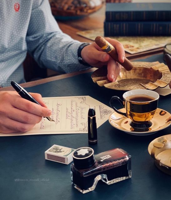 a man sitting at a table writing on a piece of paper next to a cup of coffee