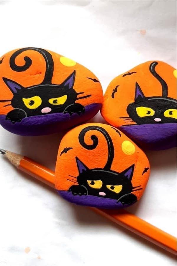 three painted rocks with cats on them and one has a pencil in the foreground