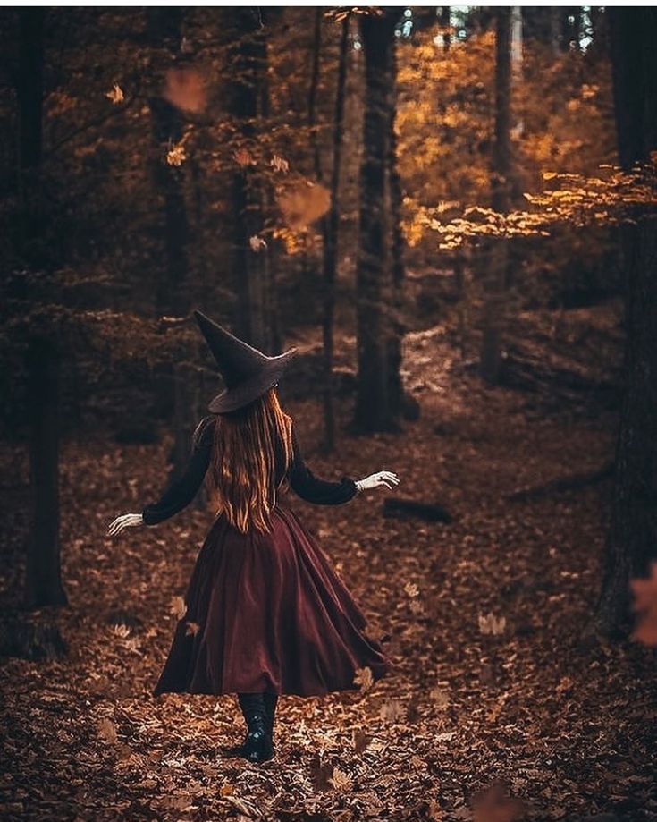 a woman in a witch costume is walking through the woods with her arms outstretched and hands out