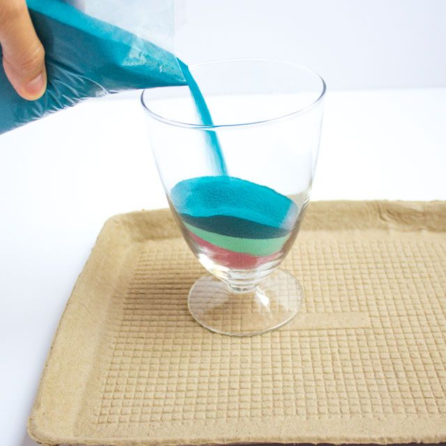 a person pouring liquid into a glass on top of a mat with a blue object in it