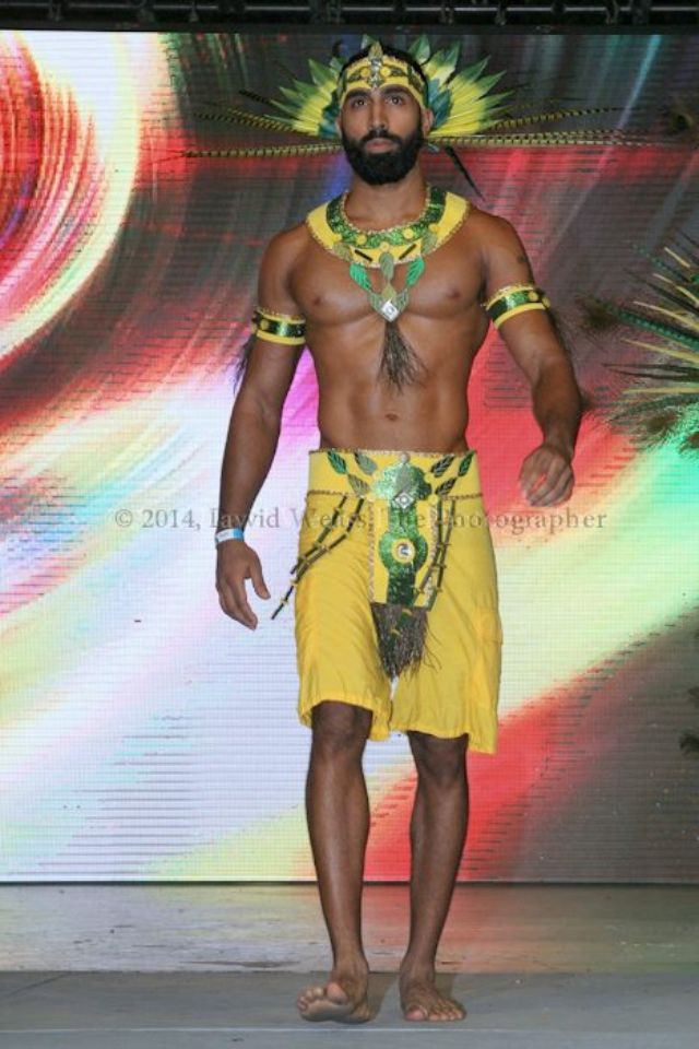 a man in yellow is walking down the runway wearing an elaborate headdress and necklace