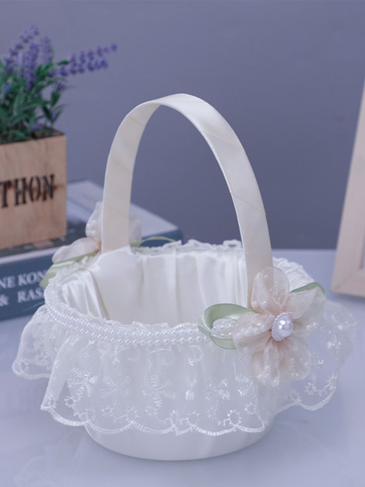 a small white basket with flowers on the bottom and lace around it, sitting on a table