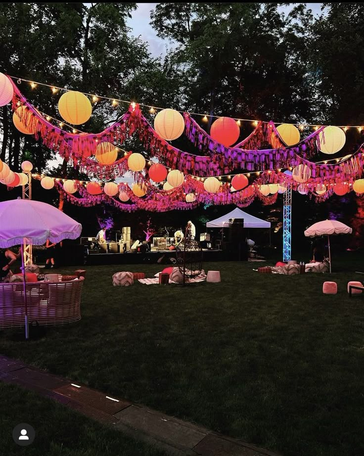 an outdoor party with paper lanterns and umbrellas on the grass, lit up by string lights